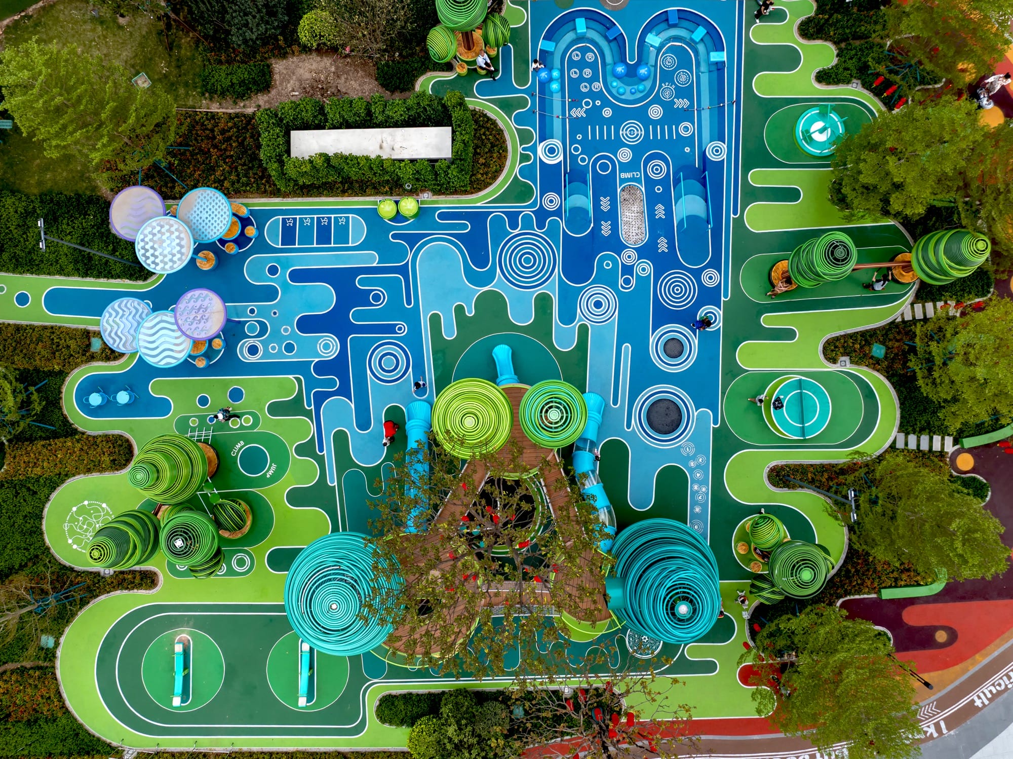 a vertical aerial overview of an elaborately designed playground with blue and green designs on the ground and wire-like sculptural trees holding up bridges and play equipment