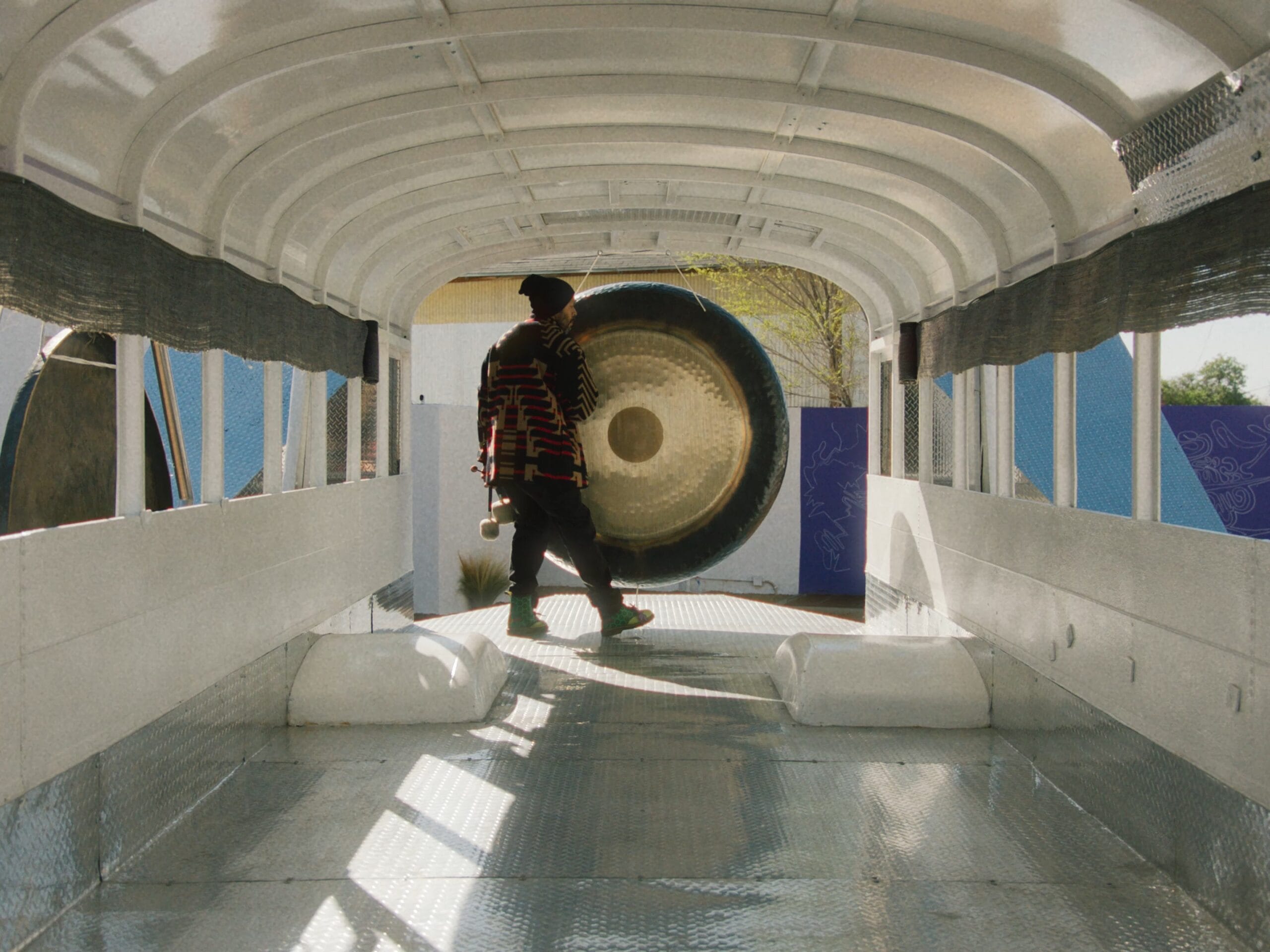 the artist standing next to a large gong in the cab of an empty bus