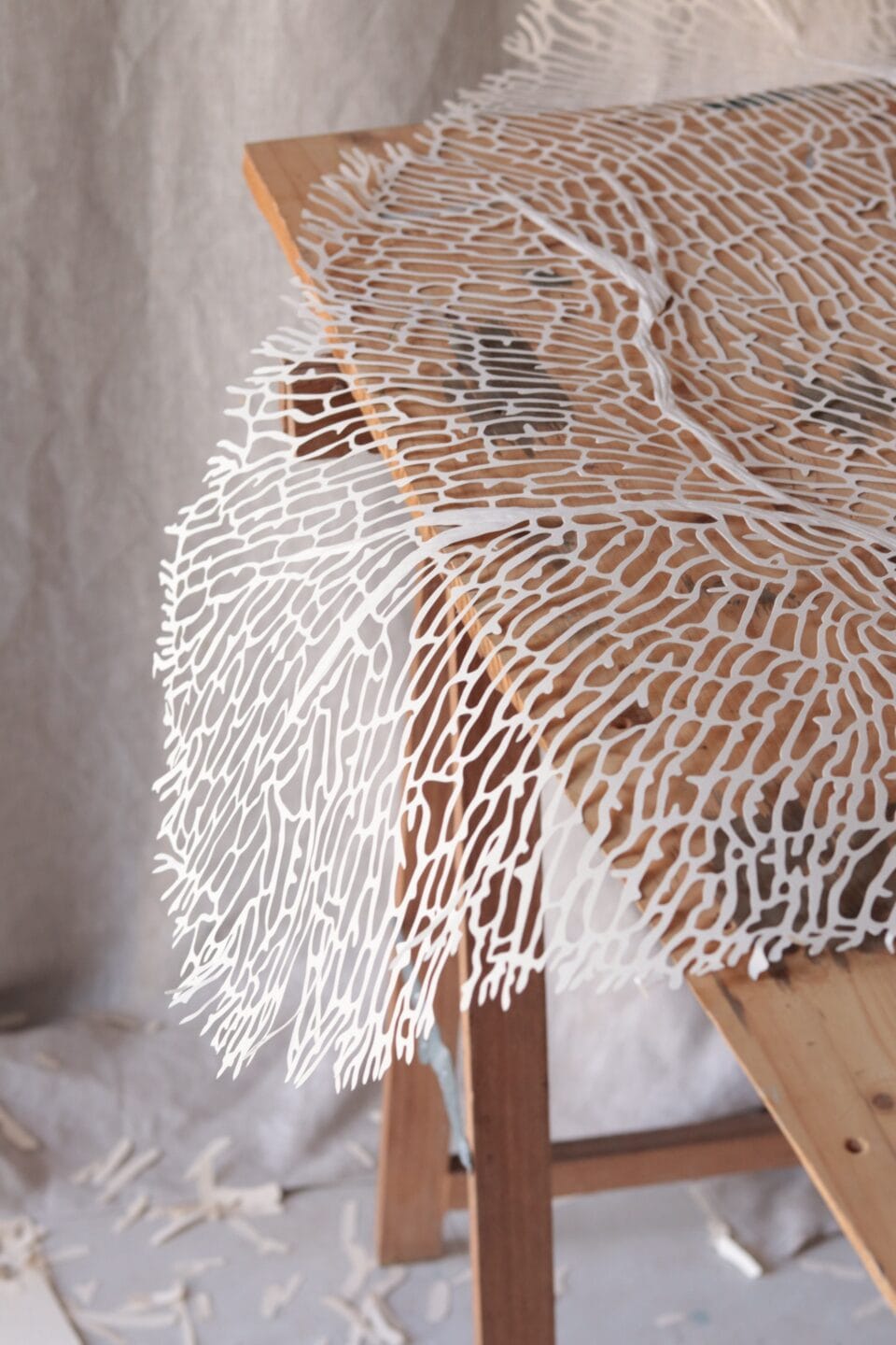 cut white material, draping off the edge of a wooden table, in the shape of coral