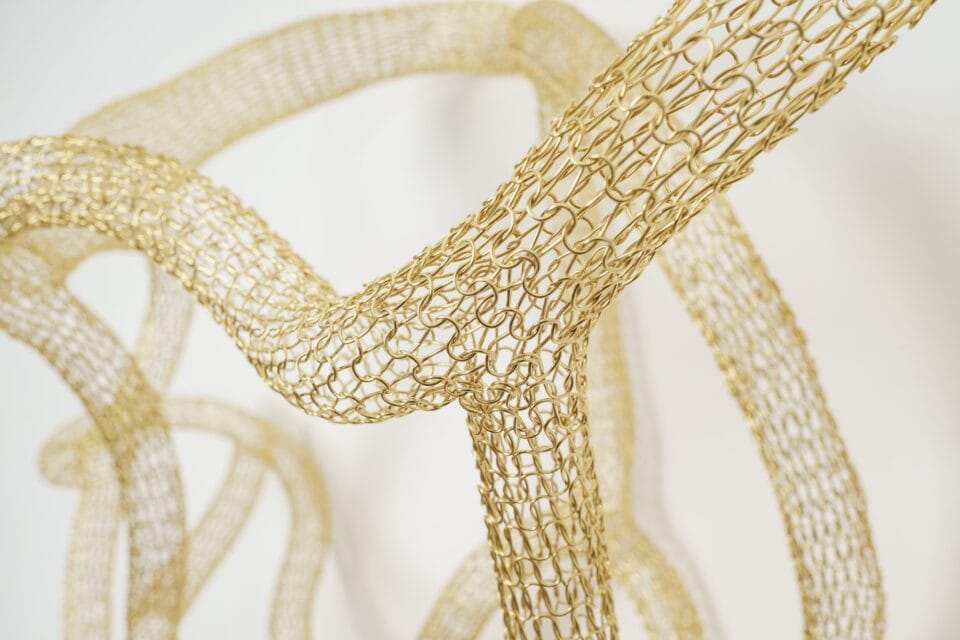 detail of a gold abstract woven metal sculpture with tubes and circular forms on a wall