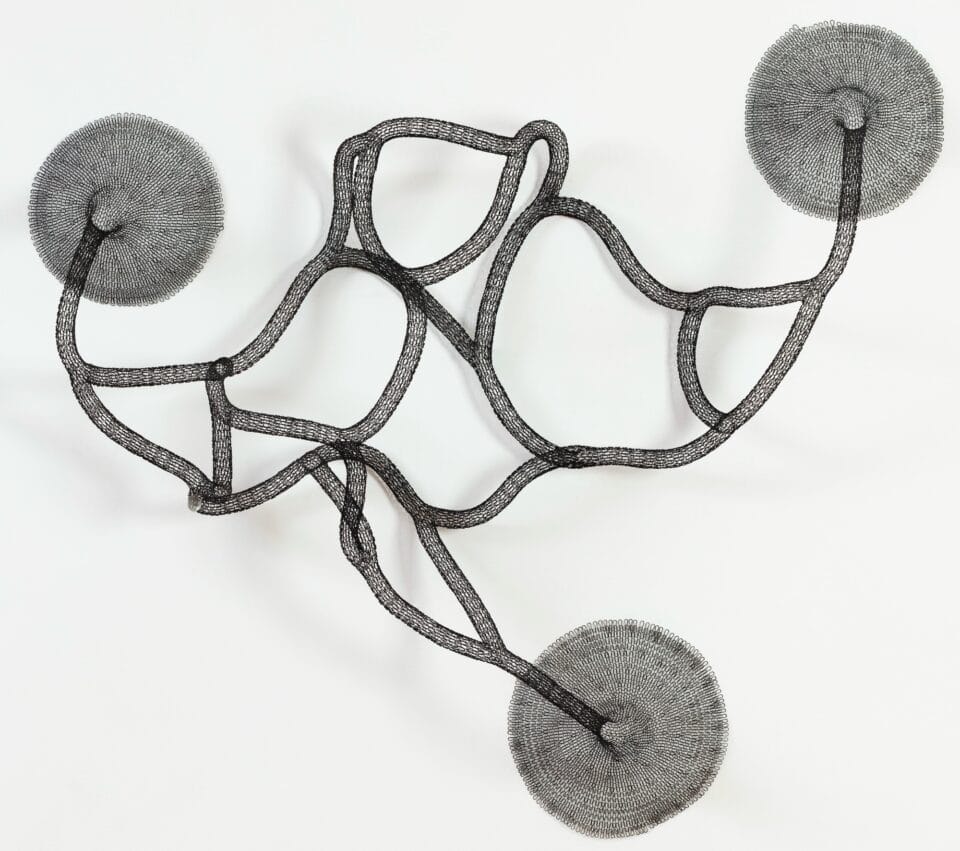a black abstract woven metal sculpture with tubes and circular forms on a wall