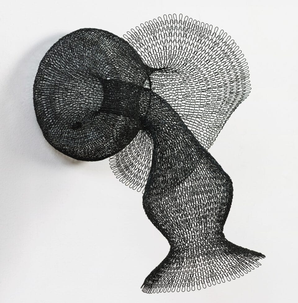a black abstract woven metal sculpture with tubes and circular forms on a wall