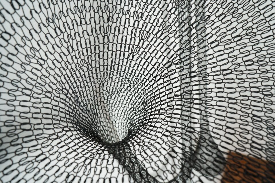 detail of a black abstract woven metal sculpture with tubes and circular forms on a wall