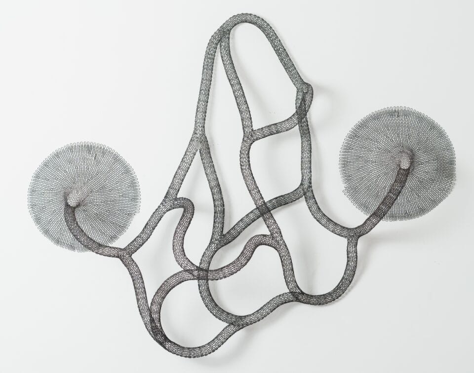 a black abstract woven metal sculpture with tubes and circular forms on a wall