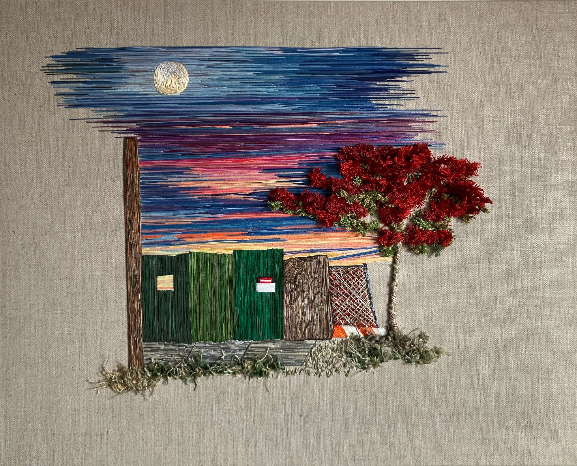 a sunset peeks over a green fence with a red flowering tree in the foreground