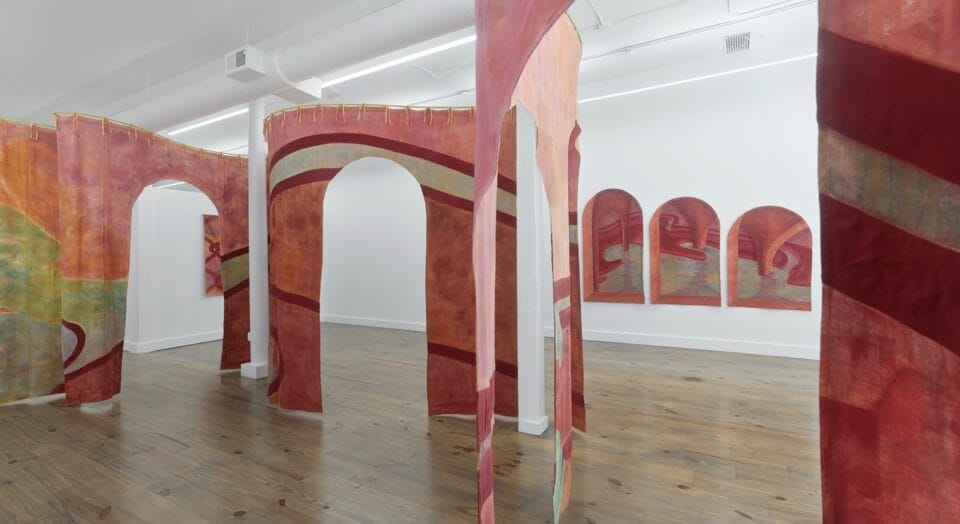 a winding tapestry in pink and green bisects a gallery. archways provide openings in the tapestry