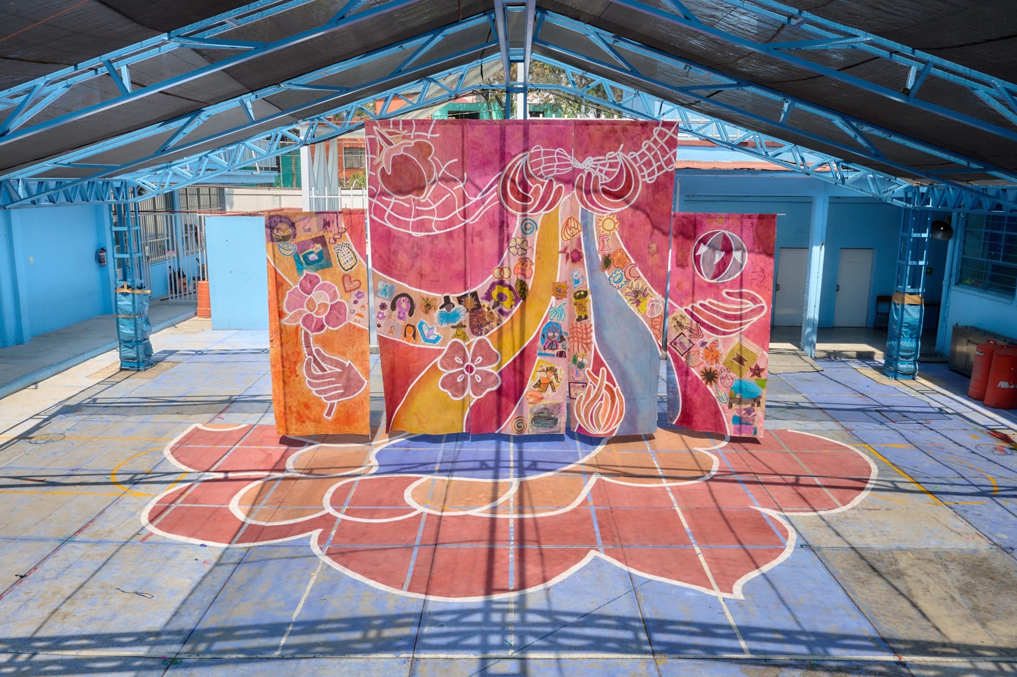 a three panel installation hangs in a large warehouse like space with pink and orange flowers painted below