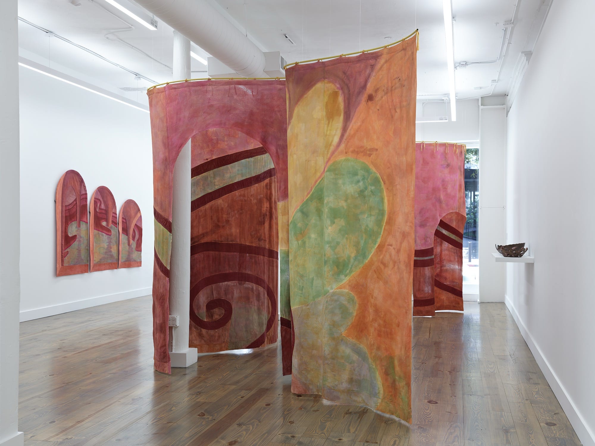 a winding tapestry in pink and green bisects a gallery