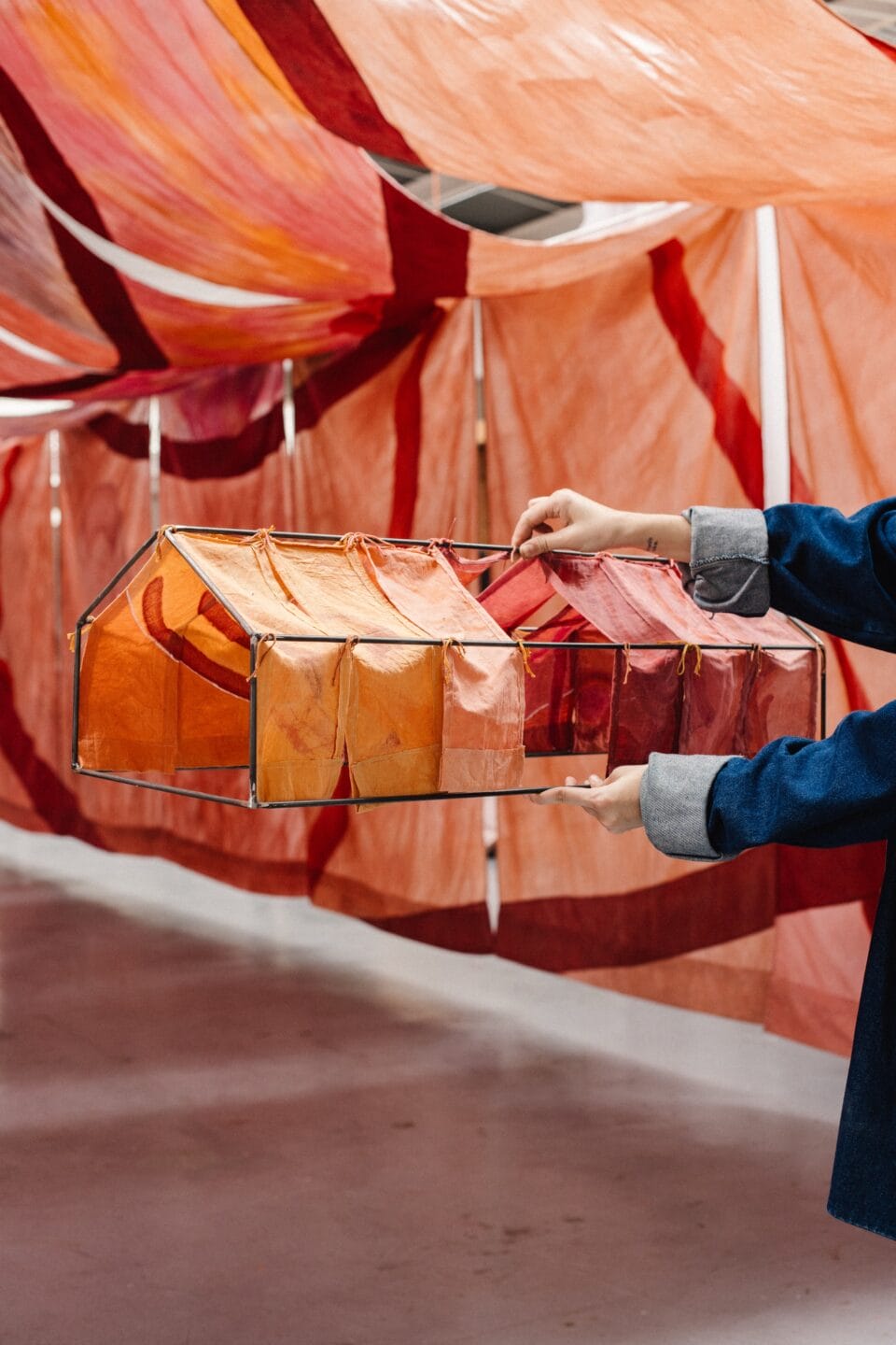 two hands hold up a structure with orange and pink fabric