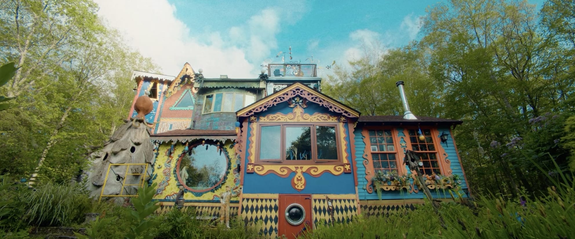 a large, whimsical house flanked by trees, painted in numerous colors with a wide variety of ornamental elements