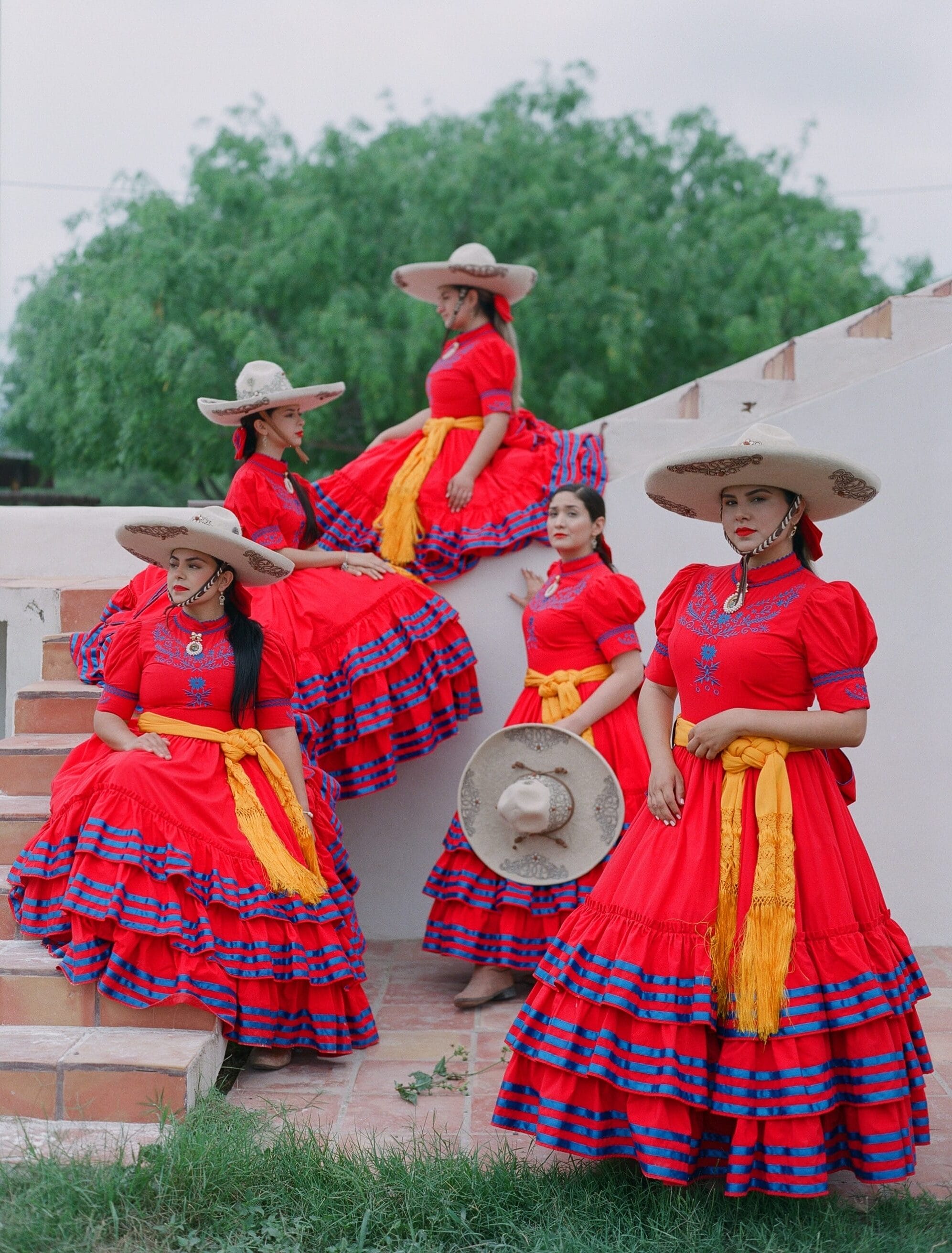 five vibrantly dressed women with wide-brimmed hats sit on some steps
