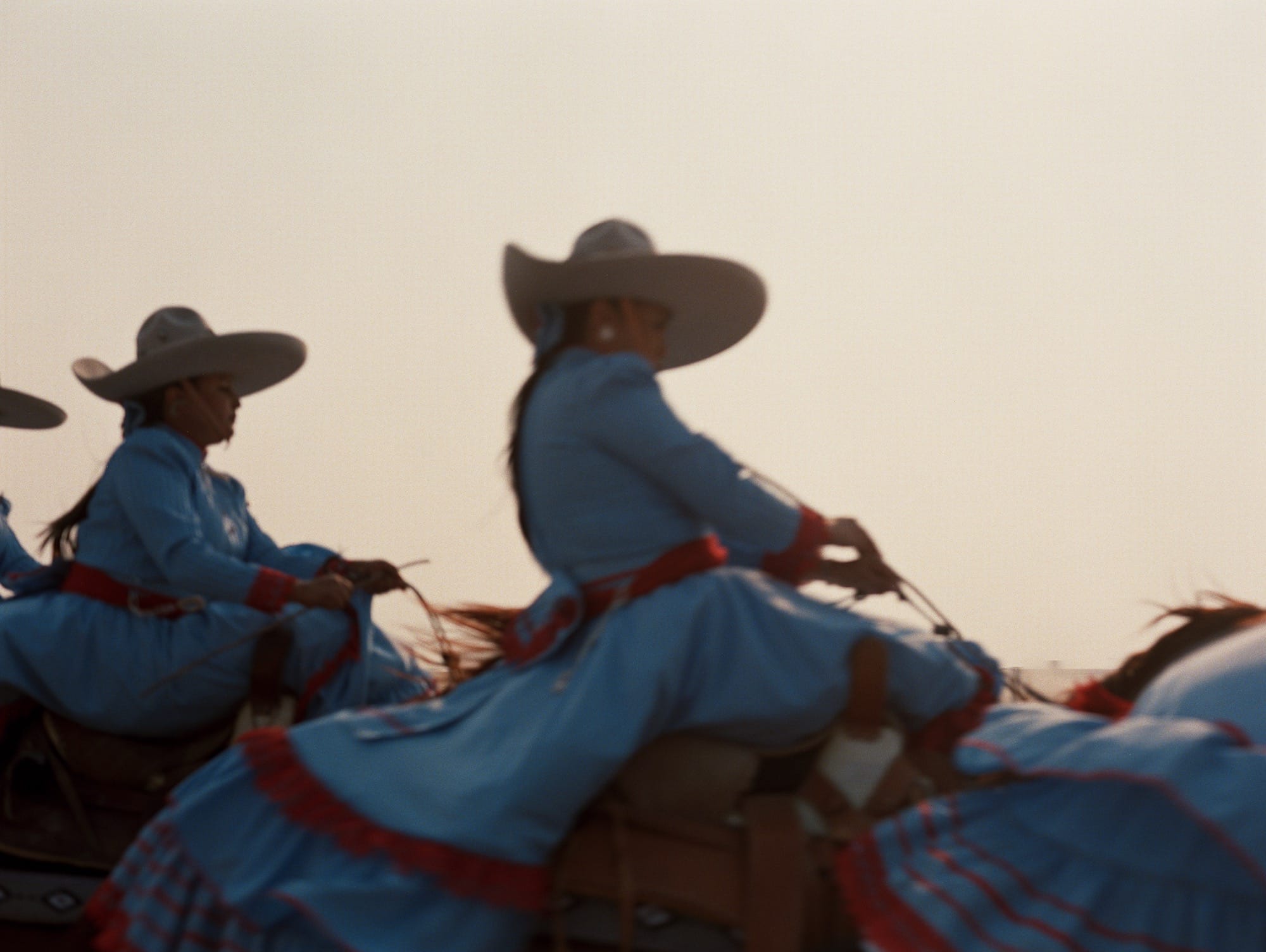women silhouetted in the late afternoon sun on horseback, wearing wide-brimmed hats