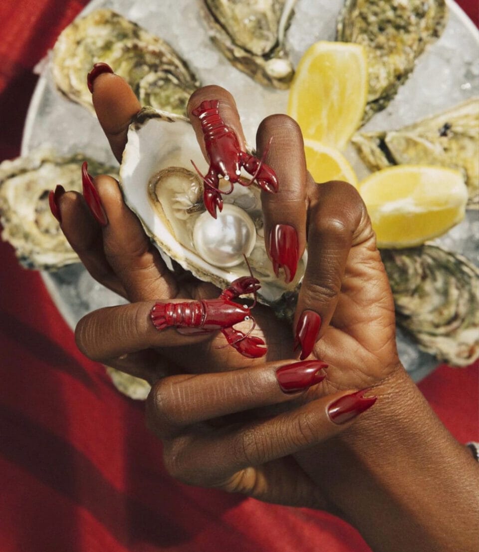 two hands hold a clam and show off a manicure with realistic lobsters and lobster claw details.