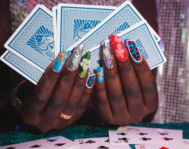 a pair of hands holding playing cards, showing off nails with intricate patterns and bright designs