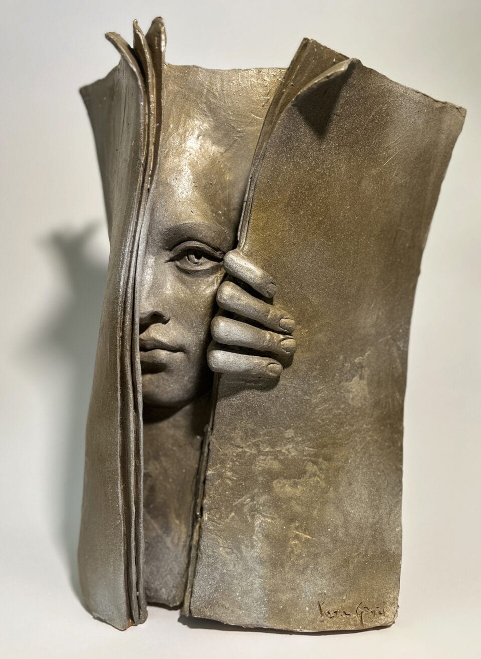 a bronze sculpture of a book or manuscript with a woman's face and hand peeking out from inside