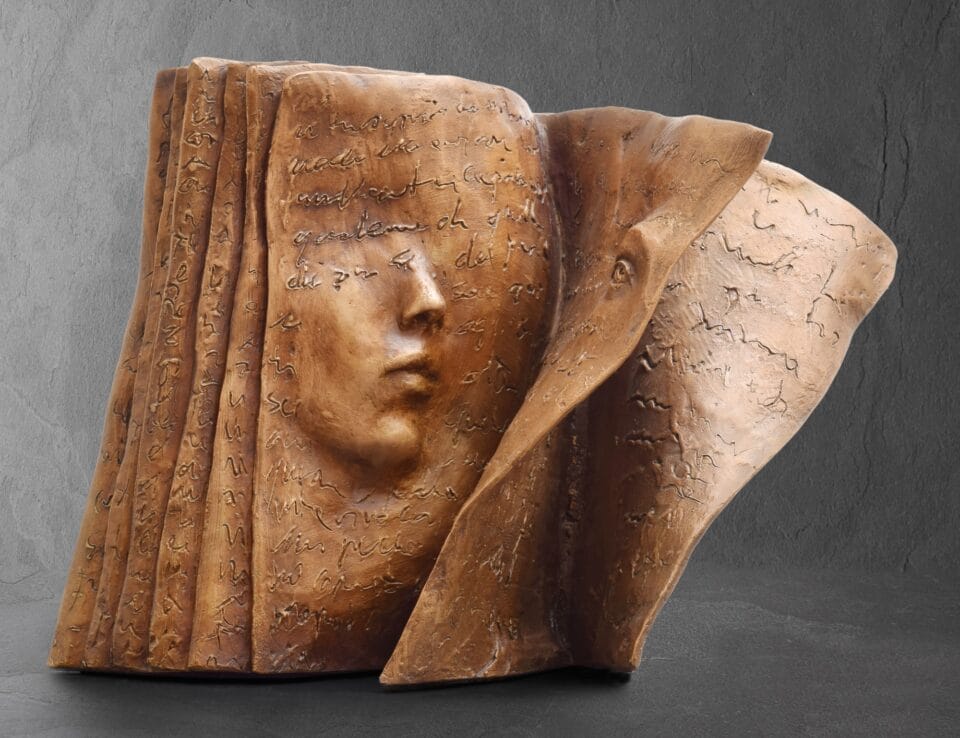 a bronze sculpture of a book with part of a woman's face in relief on the left page