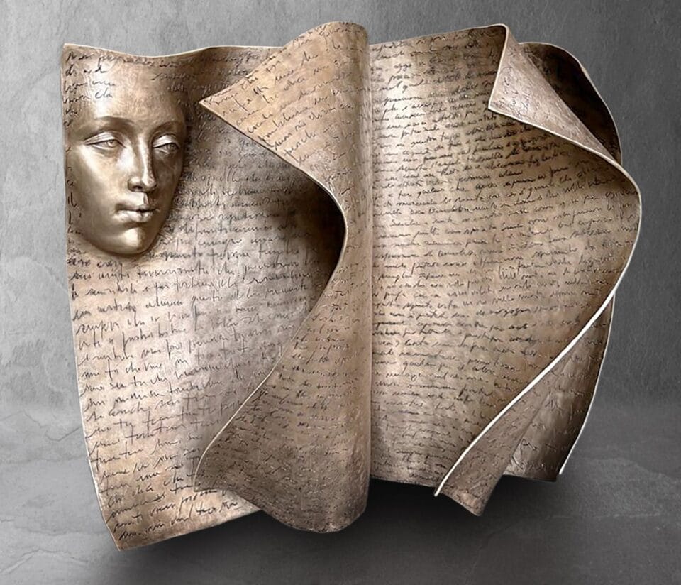 a large bronze sculpture of a book with turning pages and a face in relief on the top left