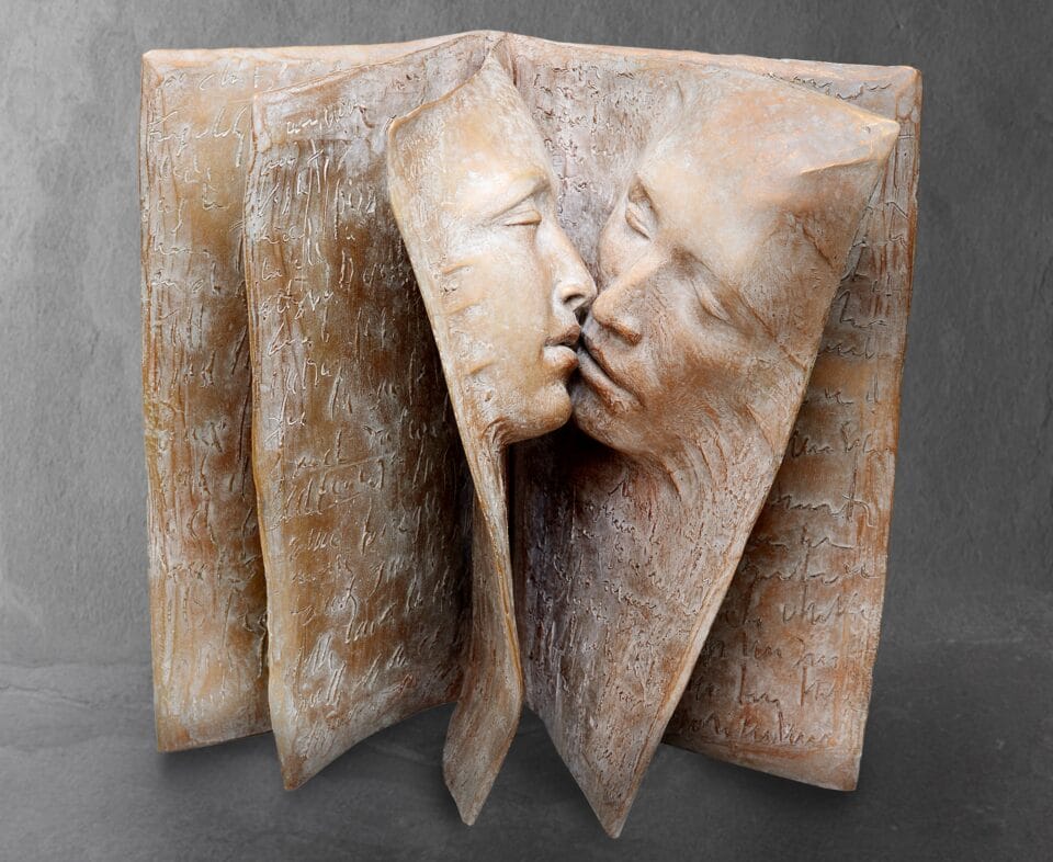a bronze sculpture of a book with two faces in relief, about to kiss