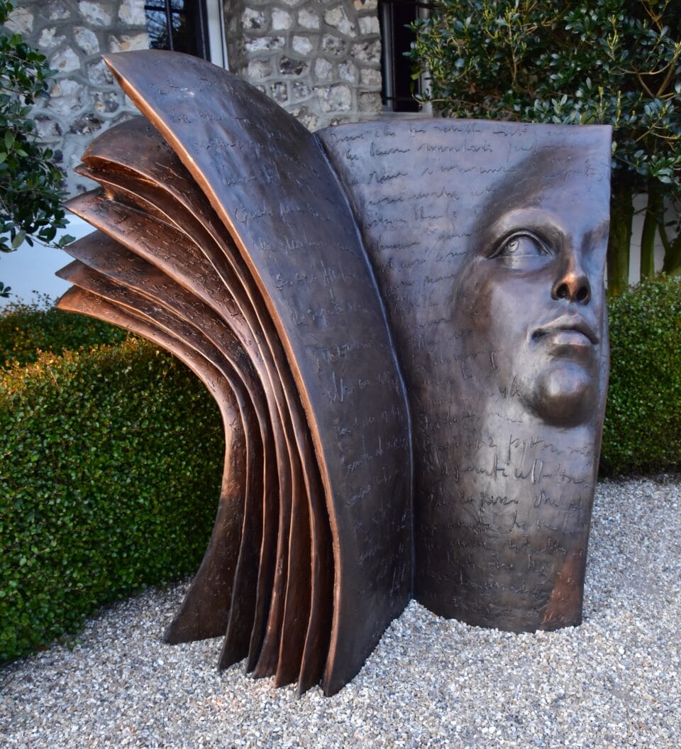 a large bronze sculpture of a book with a face in relief on one page
