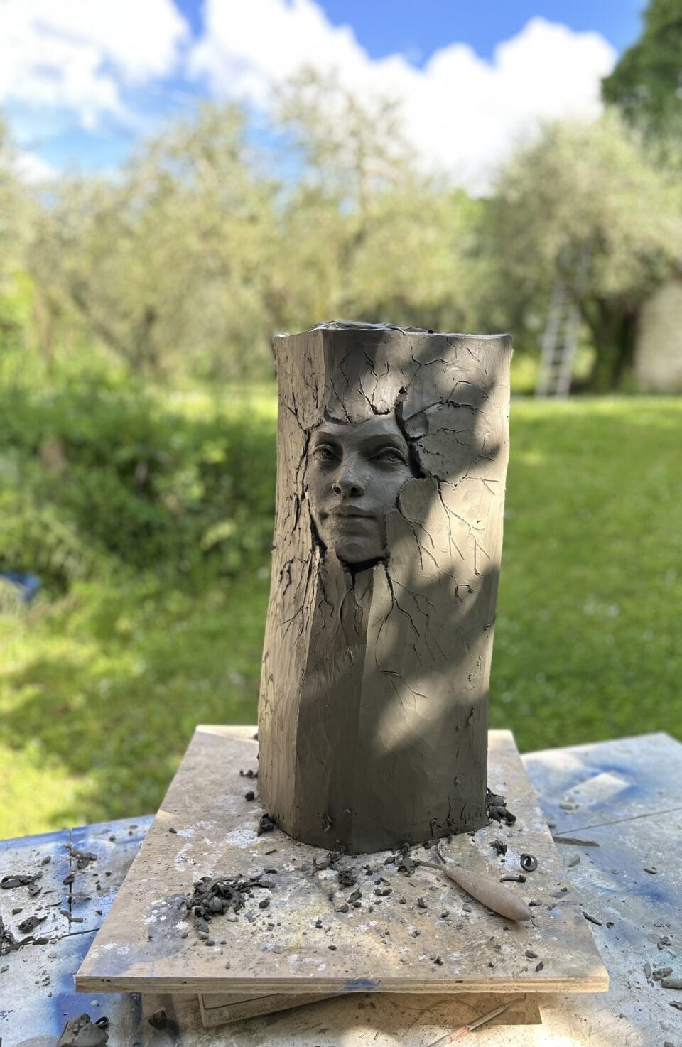a clay sculpture in progress against outdoor greenery