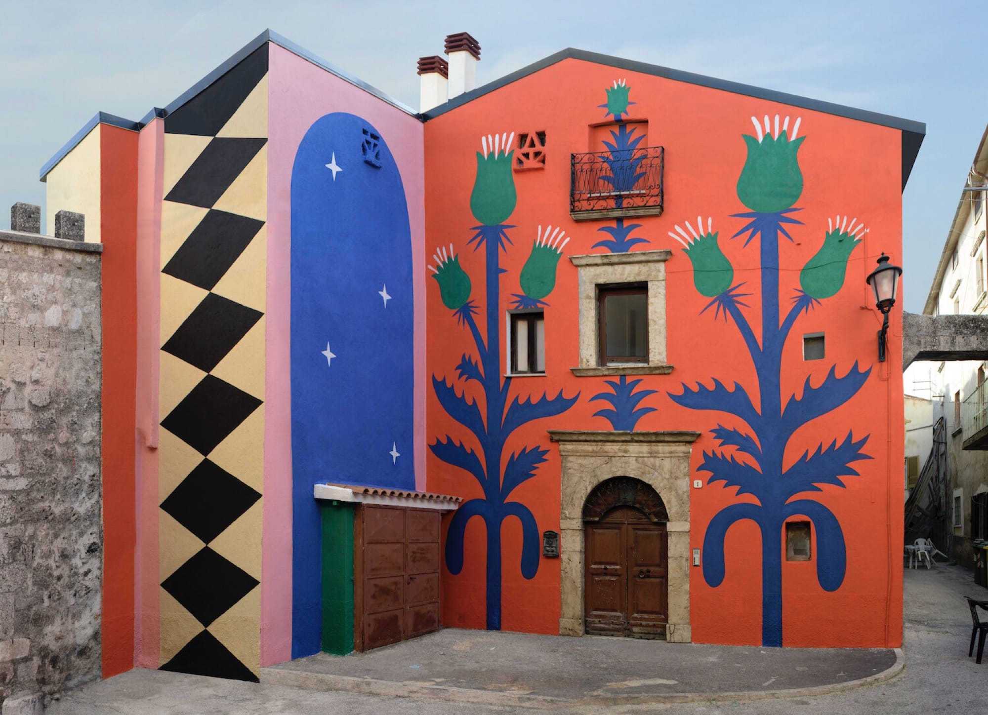 part of a mural on a two-story building in Italy, with a red background and geometric patterns and thistle designs