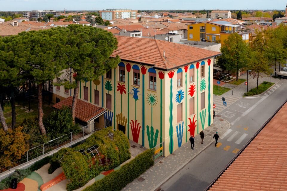 an aerial view of a building covered entirely in a colorful, geometric mural with a light yellow background and green, blue, and red patterns