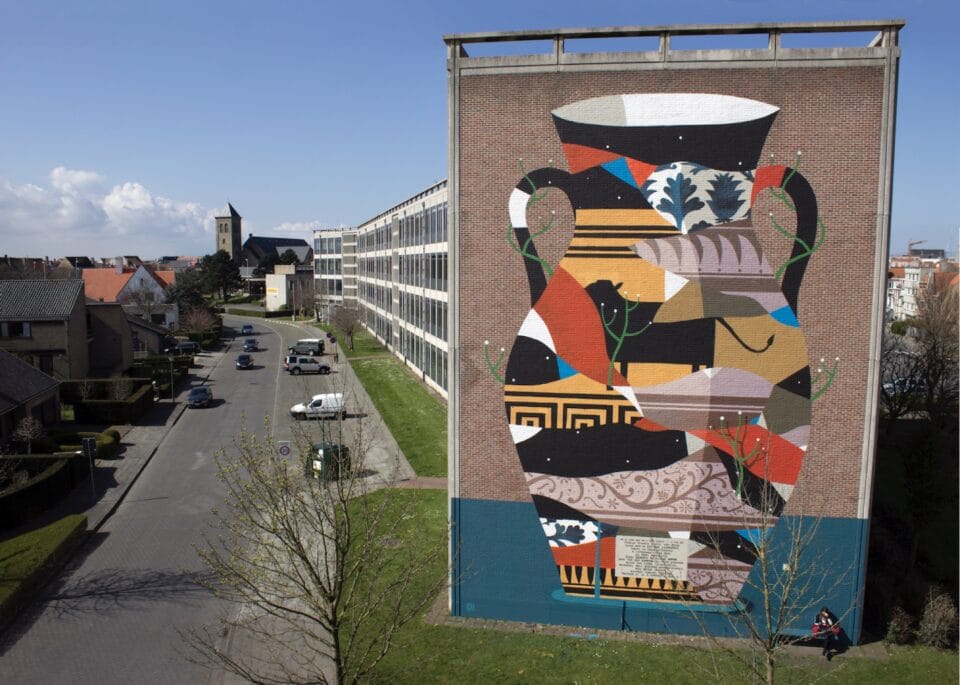 the end of a long block of apartments with a tall mural of a Greek-style vase filled with abstract color blocks and patterns