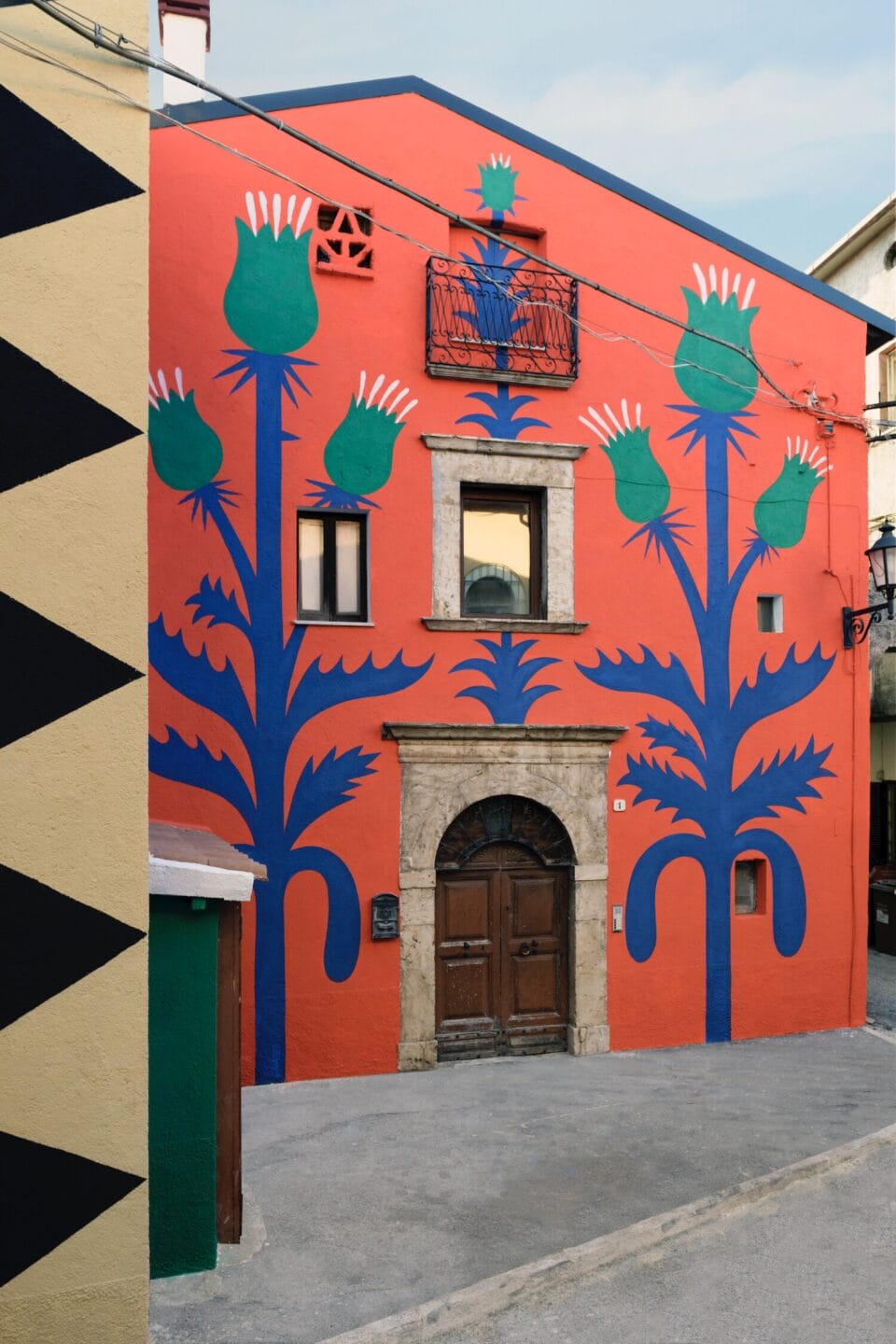 part of a mural on a two-story building in Italy, with a red background and geometric thistle designs