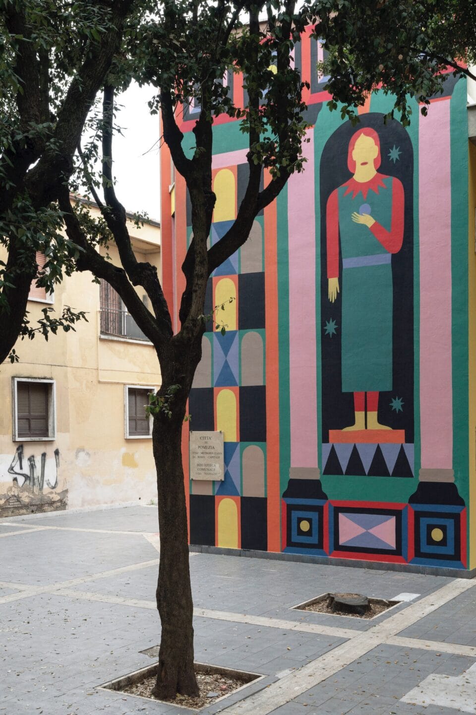 a detail of a large-scale mural on a building comprising geometric patterns and a figure in a green dress