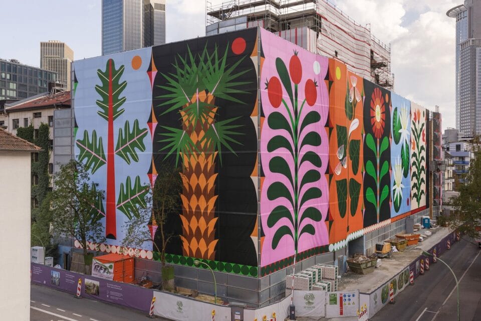 a colorfully designed fabric mural with abstract flower shapes, draped over the side of a building to mask scaffolding