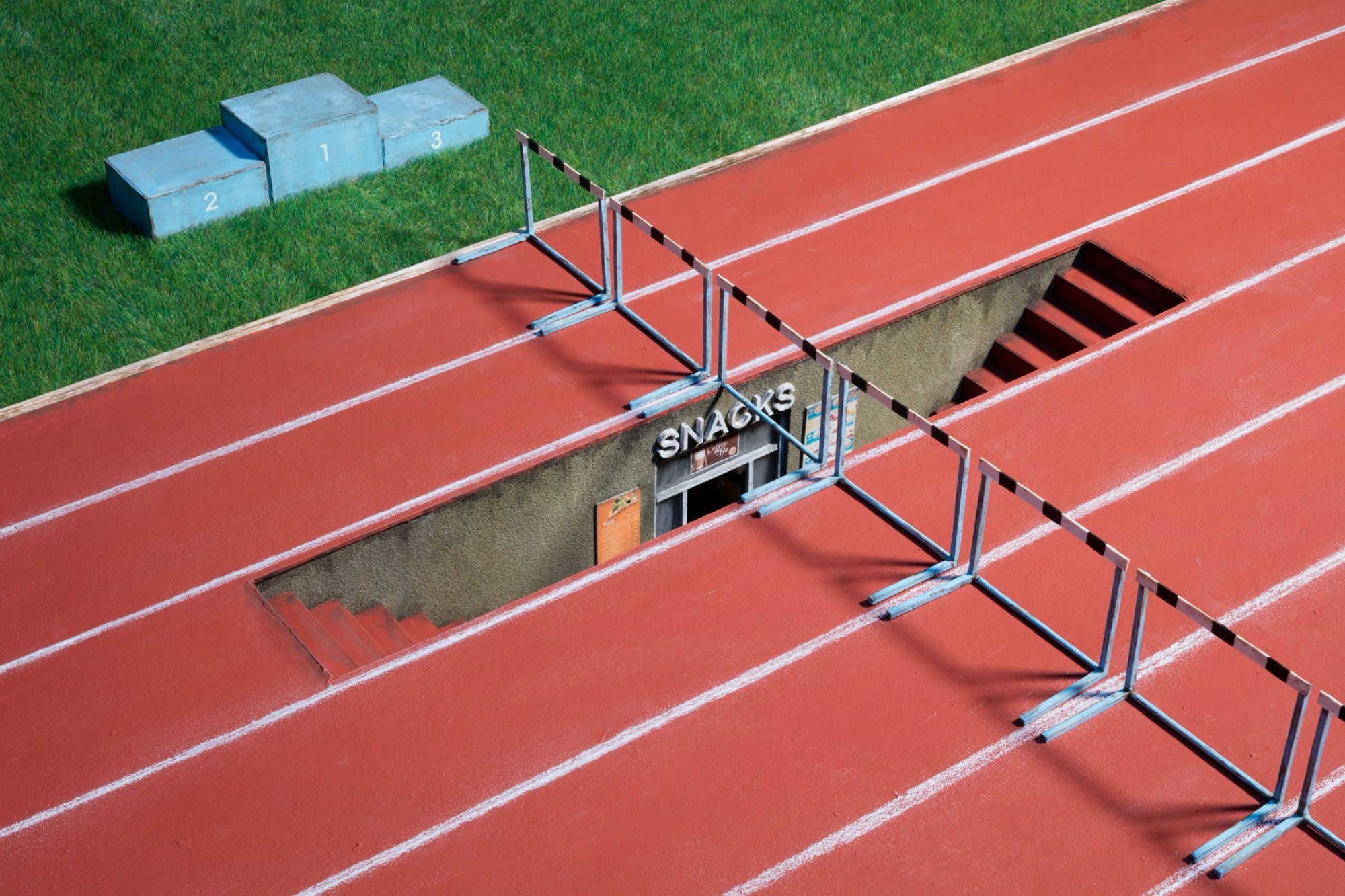 a photograph of a miniature sculpture construction of a running track with stairs leading downward in one of the lanes