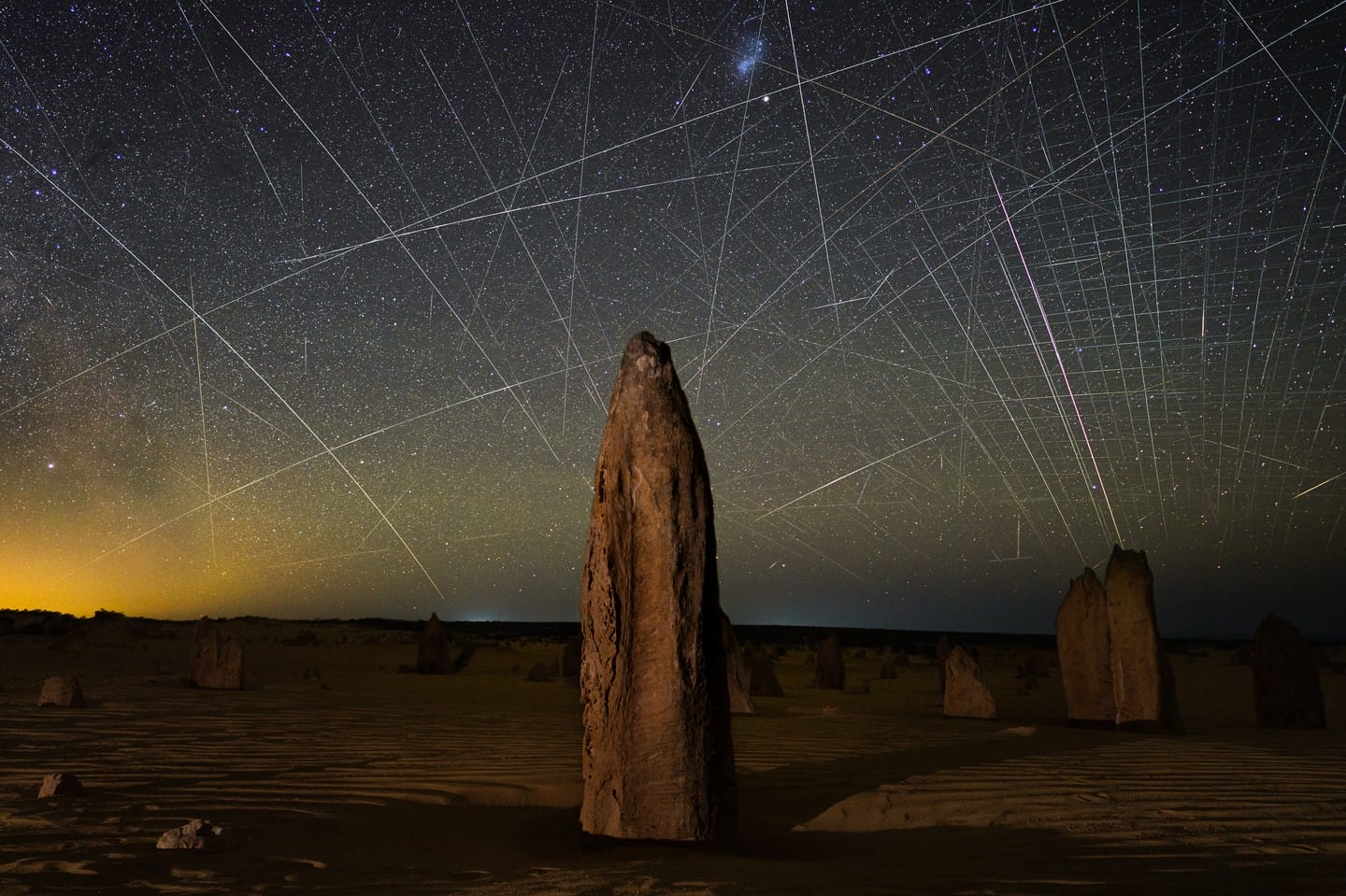 light streaks in the night sky above an arid landscape with rocky forms