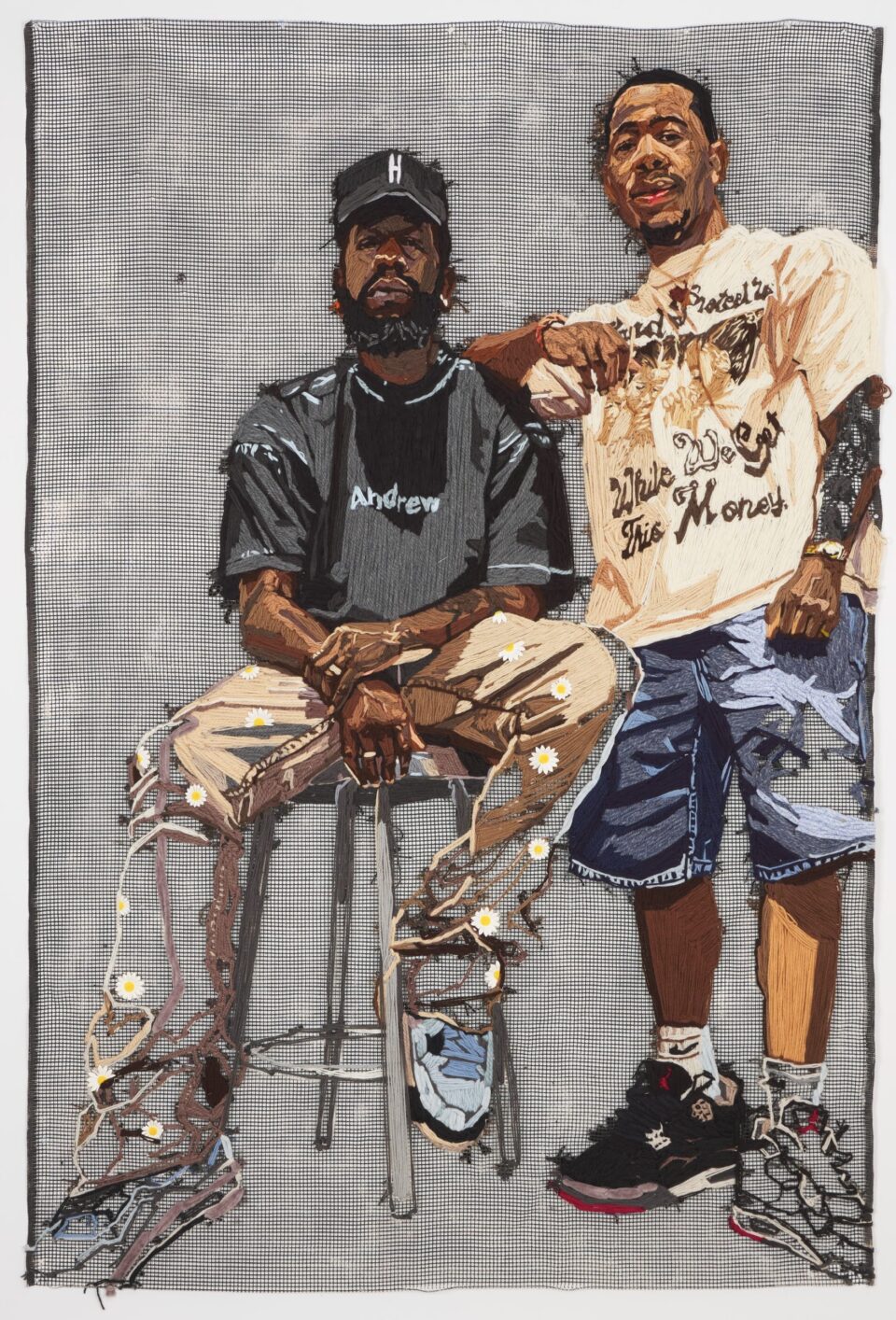 a large-scale embroidered portrait of two Black men, one seated on a stool, against a gray gridded background