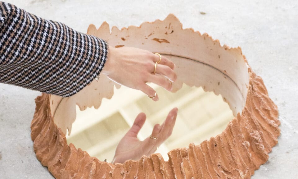 Hand hovering over a circular mirror with a 3D frame build around it to make it look like an orange crater.