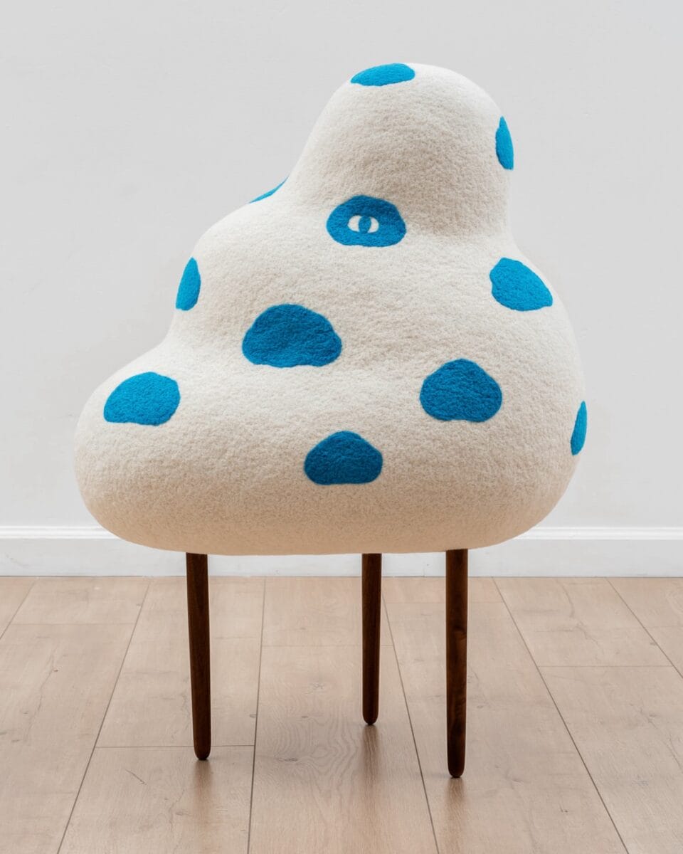 a cloud-like, abstract sculpture on spindly legs with blue cloud shapes like polka dots and a single eye