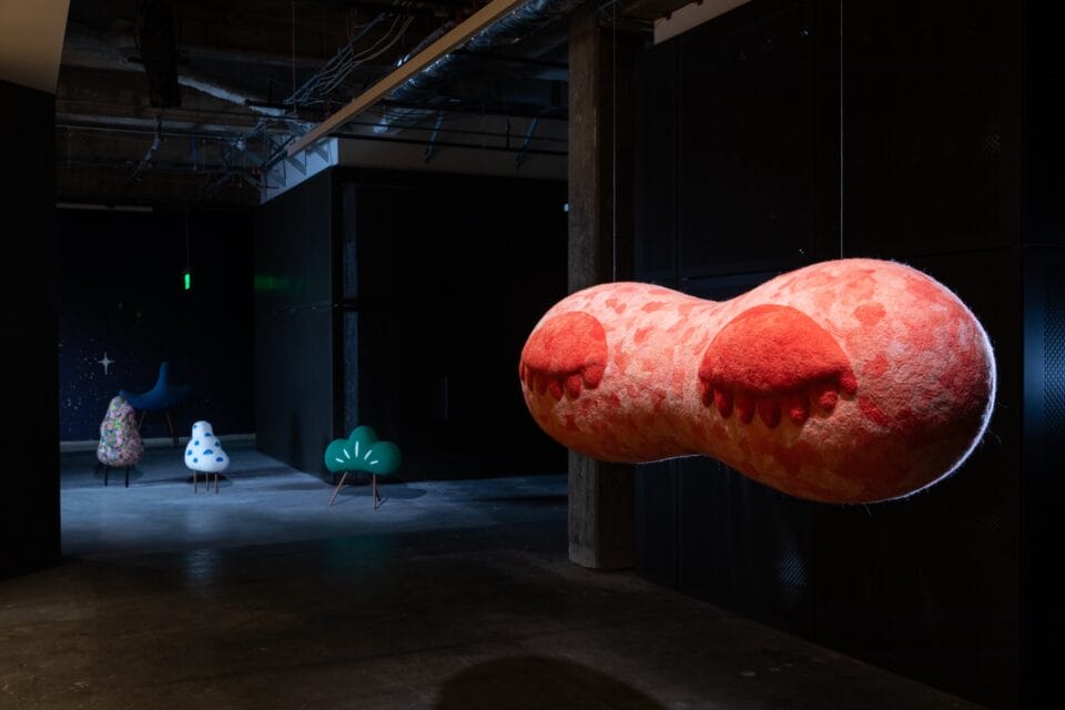 soft sculptures in a darkened gallery installation, with a suspected piece in the foreground depicting two closed eyes