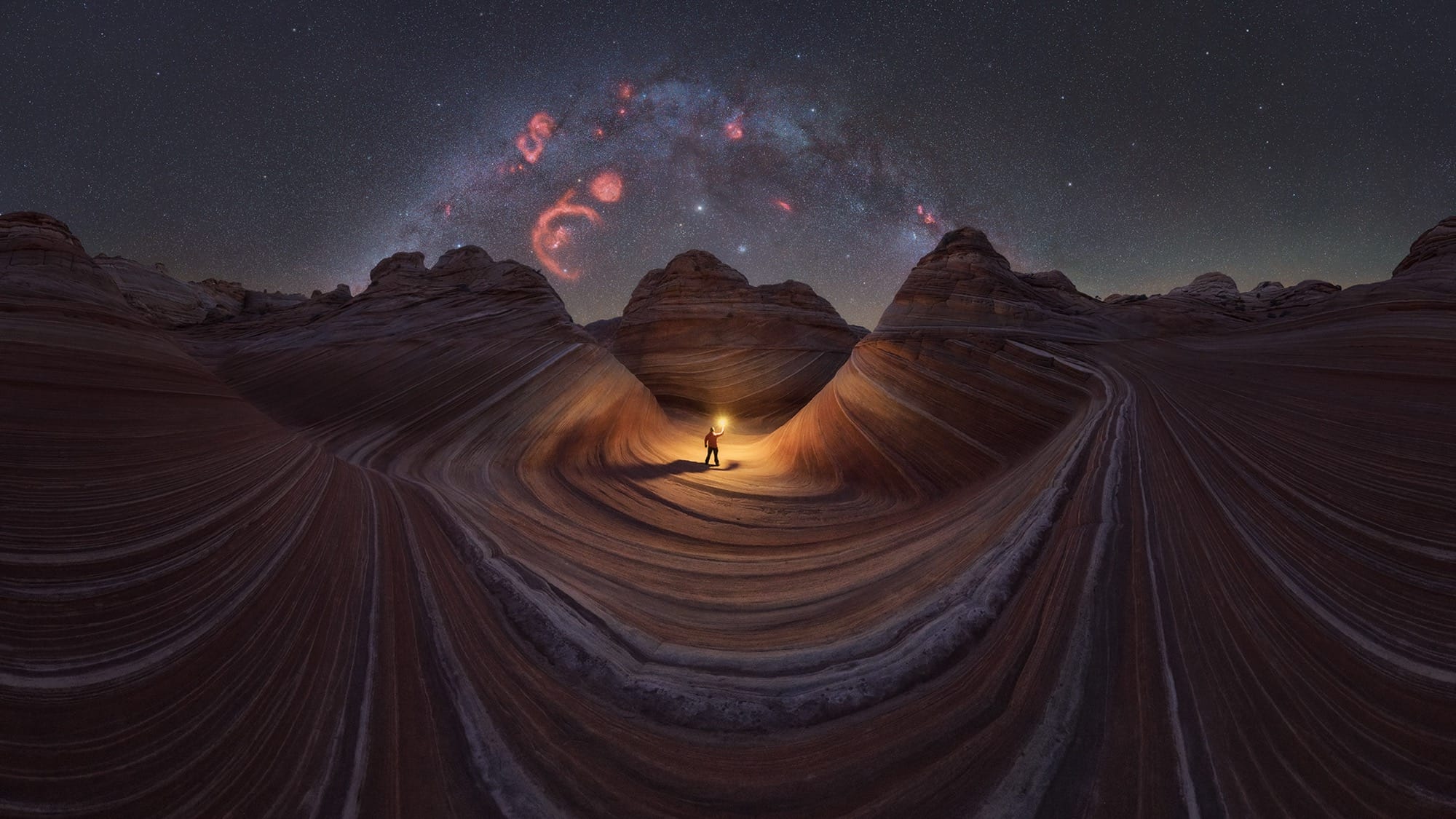 a person stands in a striped stone landscape with a light underneath the milky way