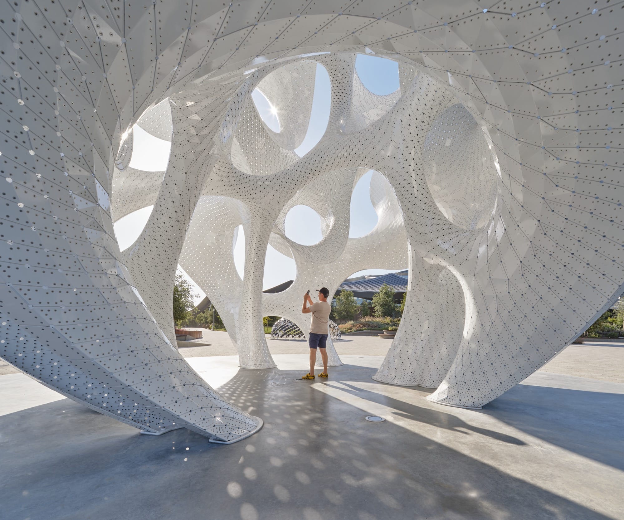 a person stands inside of a contemporary white architectural pavilion with undulating forms in the overall shape of a sphere