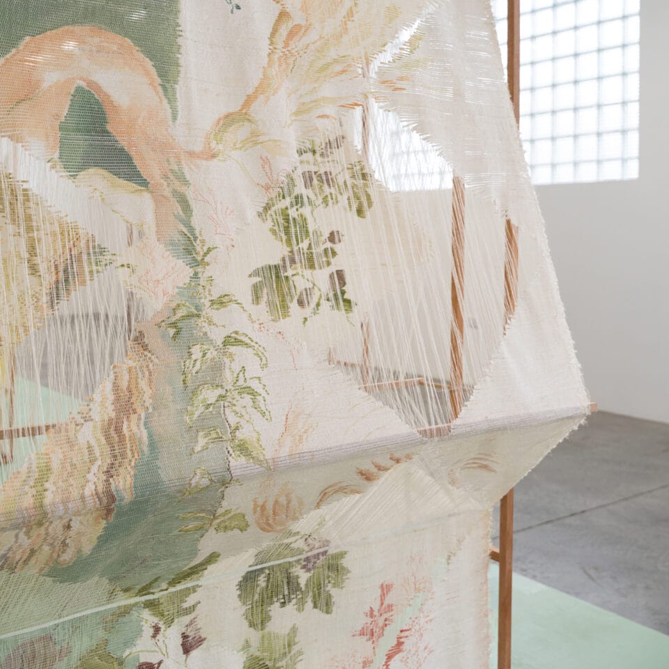 a detail of a woven, sculptural artwork in a wooden frame inside a gallery space