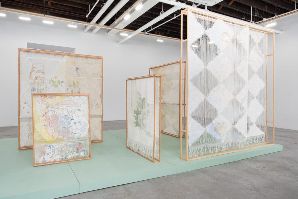 an installation of numerous woven, freestanding textile sculptures inside of a naturally lit gallery space