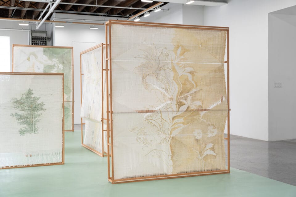 an installation of numerous woven, freestanding textile sculptures inside of a naturally lit gallery space