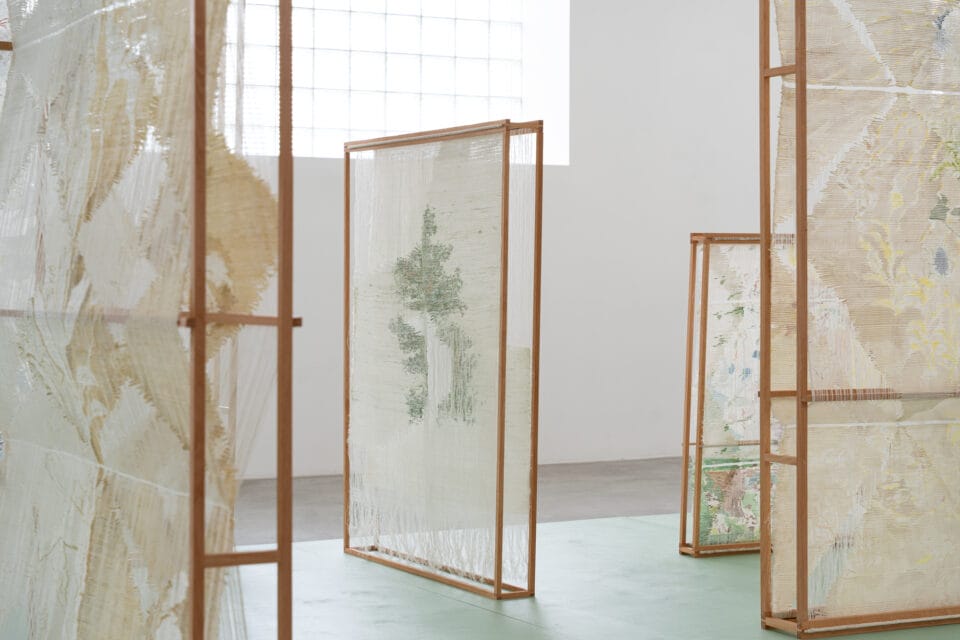 an installation of numerous woven, freestanding textile sculptures inside of a naturally lit gallery space