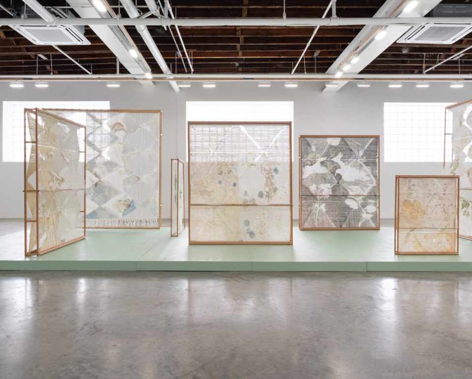 an installation of numerous woven, freestanding textile sculptures inside of a naturally lit gallery space