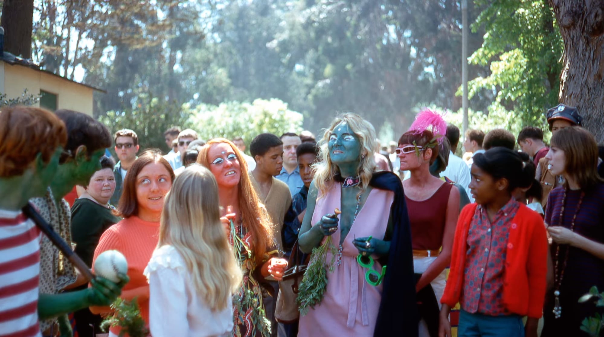 people at an outdoor gathering. several have blue or green body paint and glittery eyeshadow