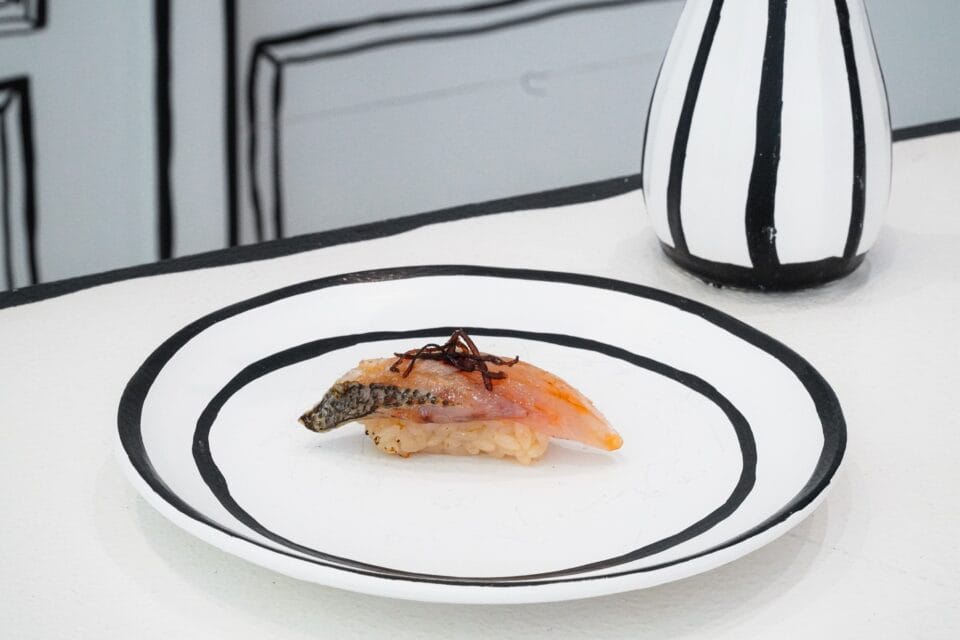 a piece of fish on a plate, on a counter, all in black-and-white to resemble a 2D line drawing