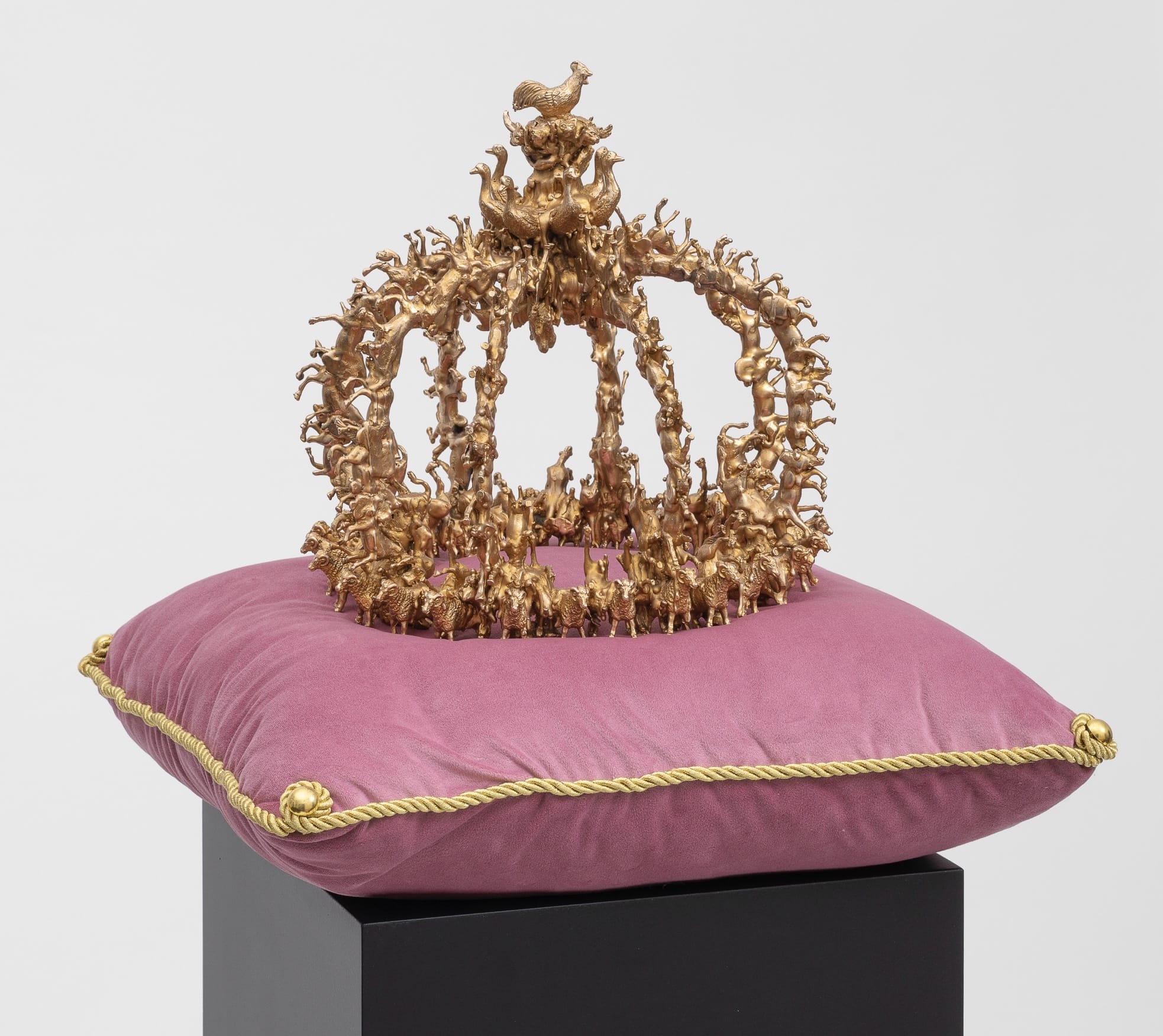 a sculpture of a bronze crown composed of tiny birds and other animals, coated in metallic silver, situated on a pink velvet cushion